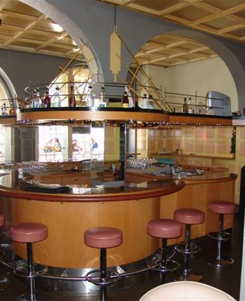 A bar counter with stools, a wooden ceiling, and a glass display case with bottles on top