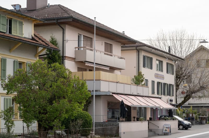 Three-story residential building with balconies, green shutters, and awnings over the storefront