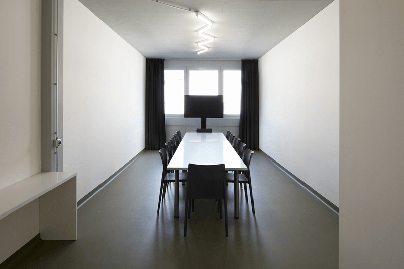 empty room, white wall, long white table, black chairs, TV, black curtains, light on ceiling