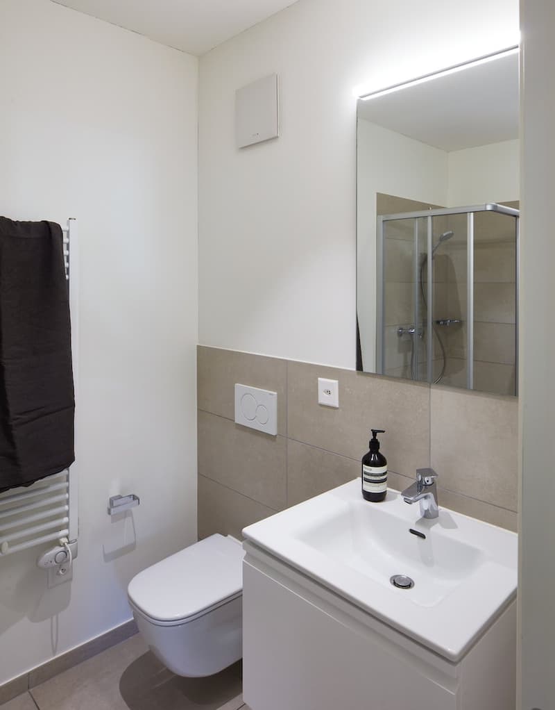 modern bathroom with white tiles, white sink, mirror, shower, toilet, towel rack