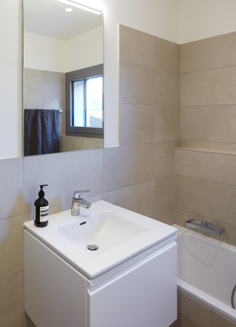 modern bathroom with white sink, mirror, bathtub, and tiled walls