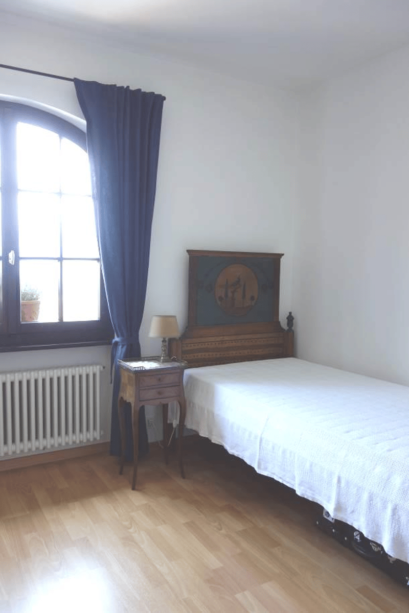 Bedroom with hardwood floor, white walls, large arched window, wooden bed frame, nightstand, and decorative wall art