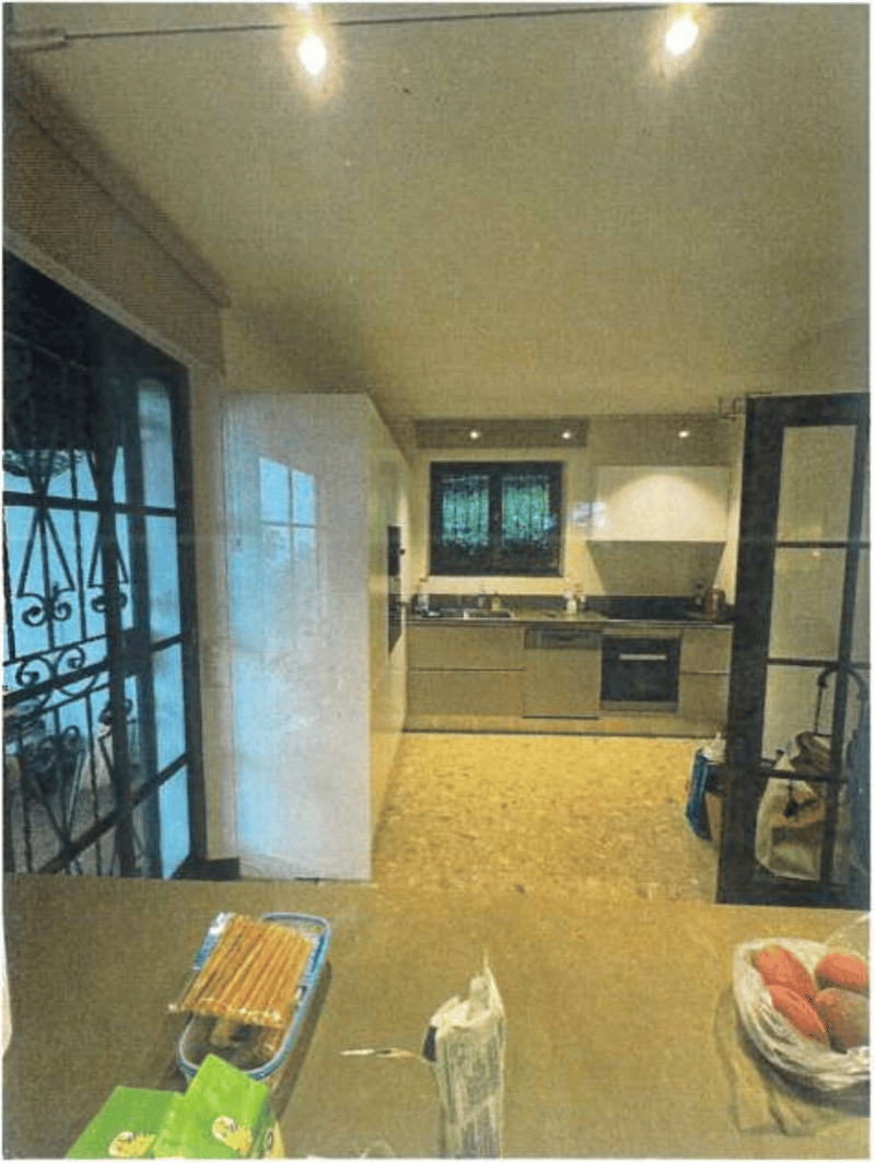 The image shows an interior kitchen with modern appliances, including a dishwasher. The kitchen has white cabinets, a stove, and a window with decorative metal bars. There are various kitchen items and utensils visible on the counter.
