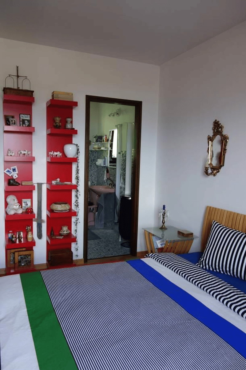 Bedroom with red shelves, bed, side table, mirror, open door to bathroom