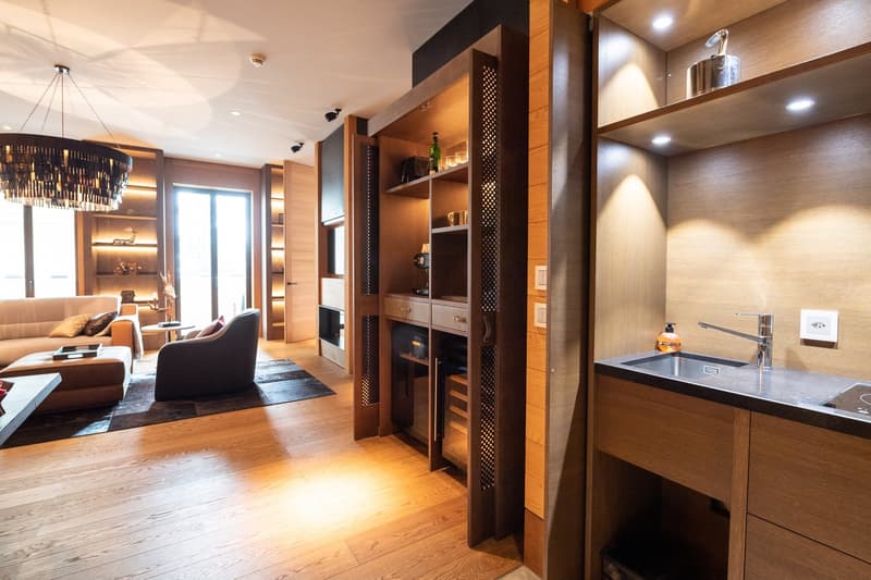 Open living area, modern interior, wooden flooring, fireplace, large windows, balcony, couch, center table, side table, wooden wine rack, sink, faucet, shelves, built-in storage, chandelier