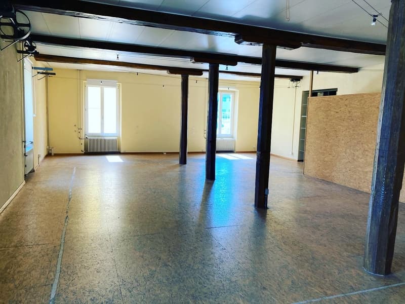 Large open space with white ceiling, wooden pillars, and wooden flooring, radiators, two windows