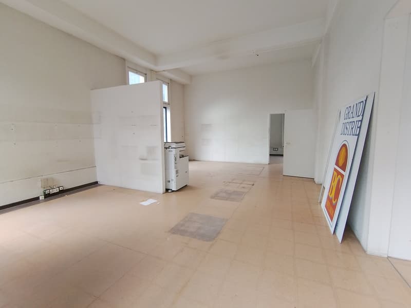Large empty room, white walls, white ceiling, tiled floor, windows with white frames, a printer against the wall, an open door leading to another room