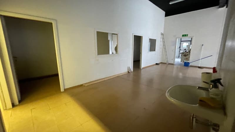Empty room, tiled floor, white walls, mirror, small sink, roll of toilet paper, white spray bottle