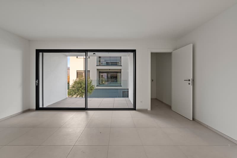 Spacious room with large sliding glass doors, white walls, and tile flooring. The room has a minimalist and modern design aesthetic.
