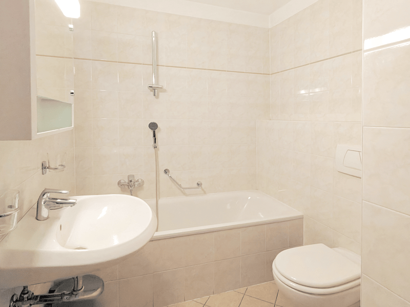 White bathroom with tiled walls and floors, a bathtub, a white sink with faucet, a white toilet, and a shower.