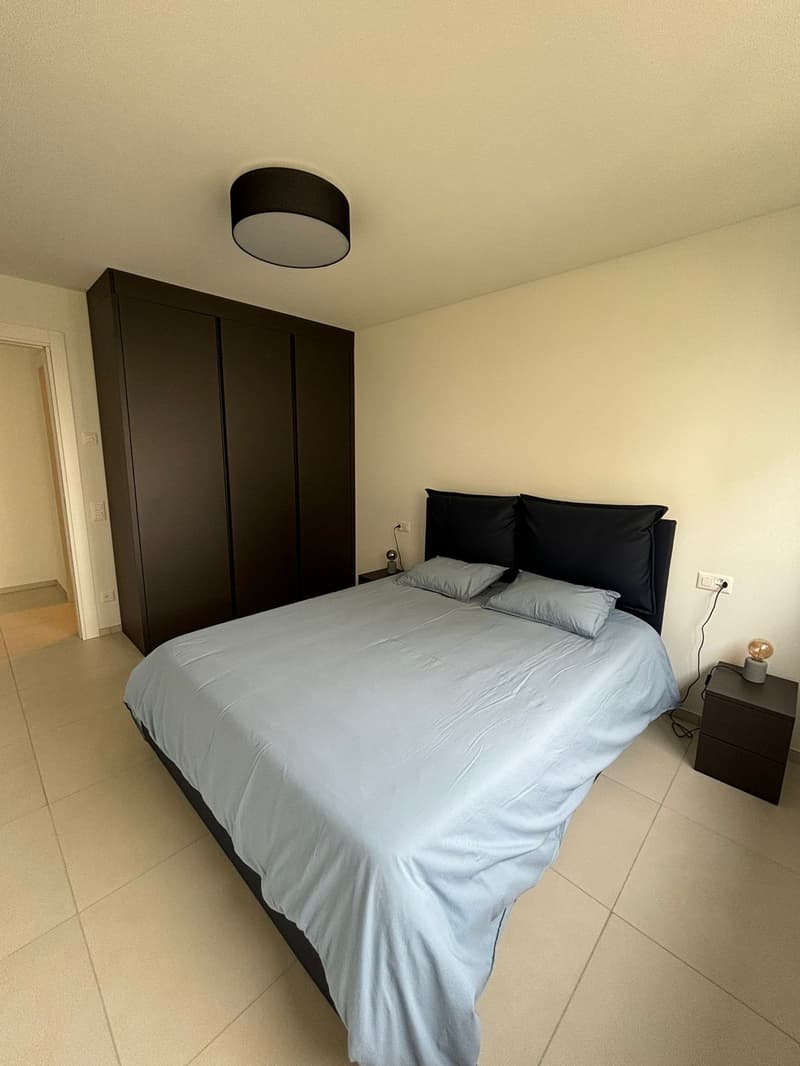 large bed, blue bedding, wooden nightstands, ceiling lamp, wardrobe, power outlet, tiles floor