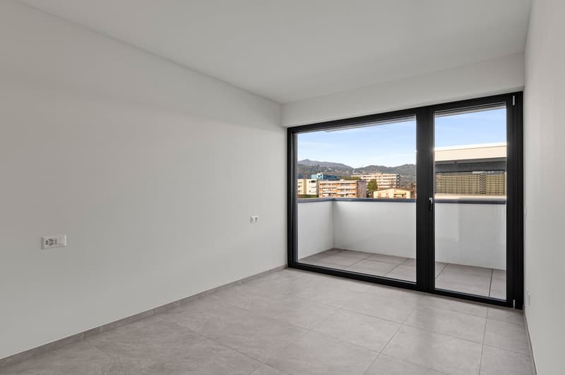 Spacious bedroom with large windows, sliding glass door leading to a balcony, and tile flooring.