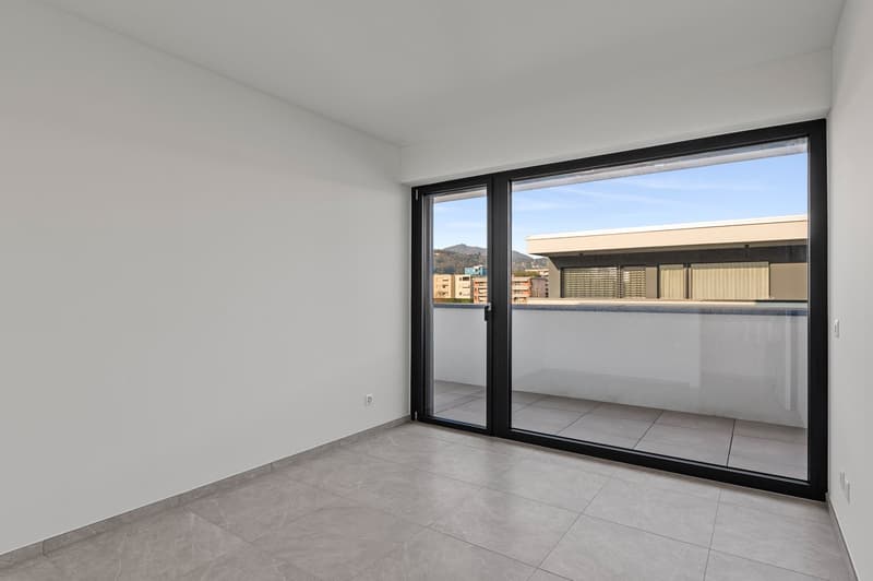 Empty room with tile flooring, large glass sliding doors to a terrace, city view, and a power outlet