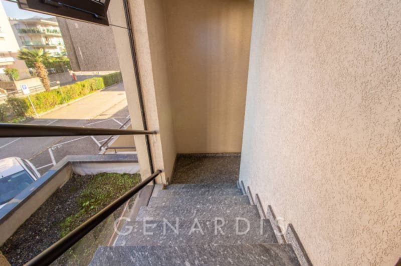 Marble staircase with black handrail, leading to a raised ground floor