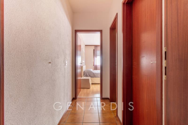 Empty hallway with wooden doors, tiled floor, bedroom with bed and window
