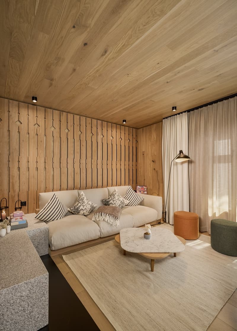 Living room with wooden walls, beige sofa, marble coffee table, beige rug, floor lamp, white curtains