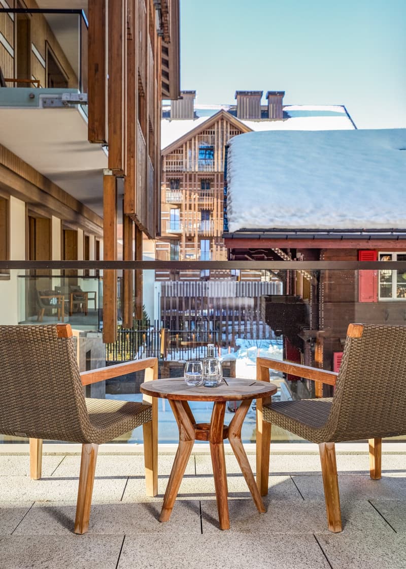 wooden chairs, round table, glass railing, snow-covered roofs, distant buildings