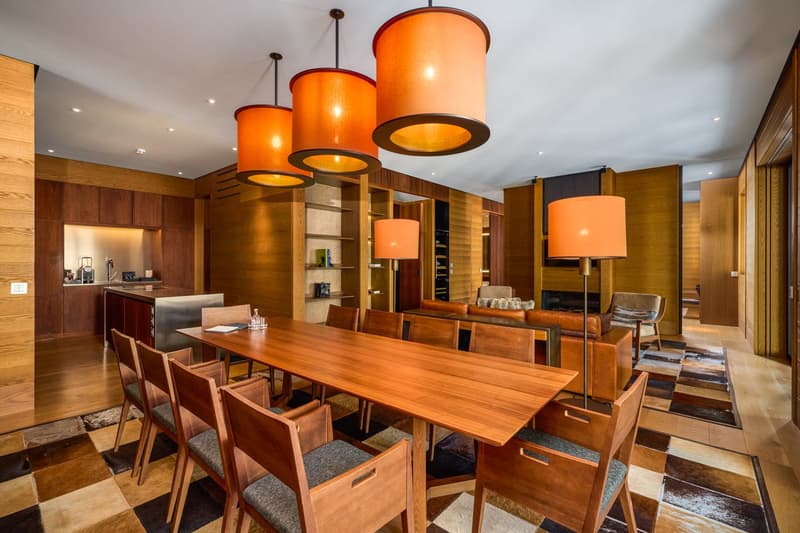 Dining room with wooden table, wooden chairs, wooden cabinets, orange lamps, carpet, kitchen area