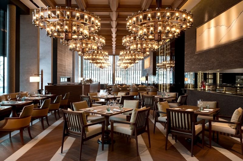 A restaurant with wooden floors, chandeliers, tables, chairs, and a bar counter.