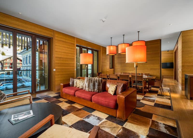 living room with wooden walls, large windows, leather couch, dining table, lamps