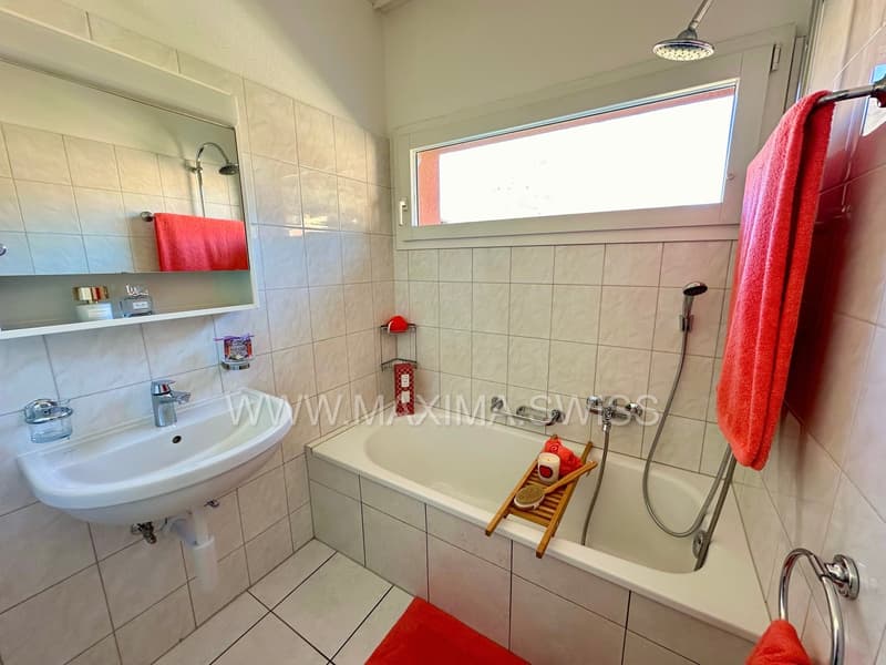 white bathtub, white sink, mirror, red towels, white tiles