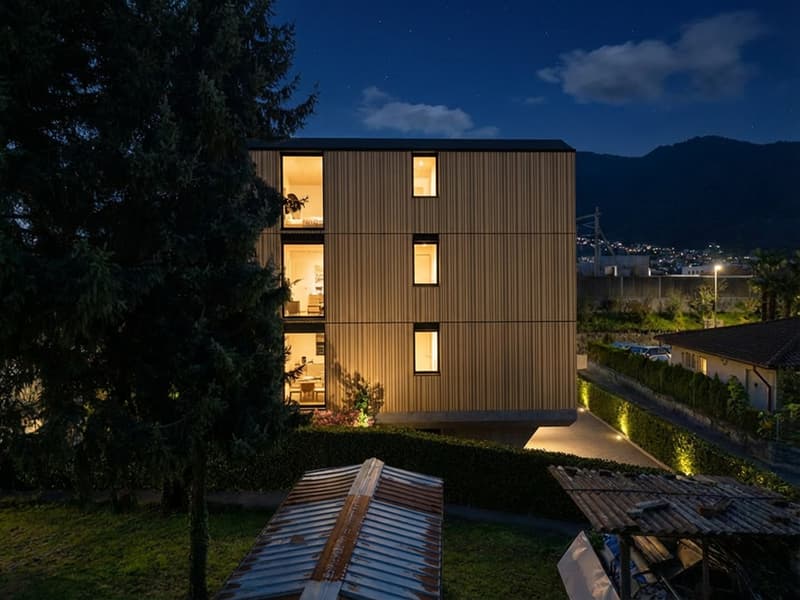 modern wooden house, 3 floors, large windows, illuminated at night, surrounded by greenery