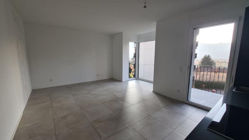 Spacious living room with large windows, sliding glass door leading to a balcony, and gray tile flooring.