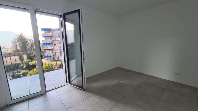 Spacious living room with large windows, sliding glass door leading to a balcony, and tiled flooring.