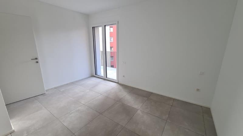 Spacious bedroom with white walls, large windows, and gray tile flooring.