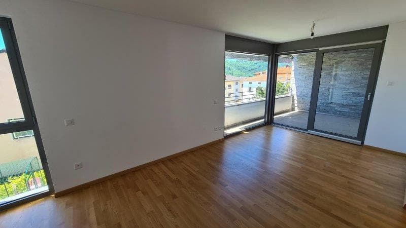 Empty room with wooden floors, white walls, and large glass doors leading to a balcony.