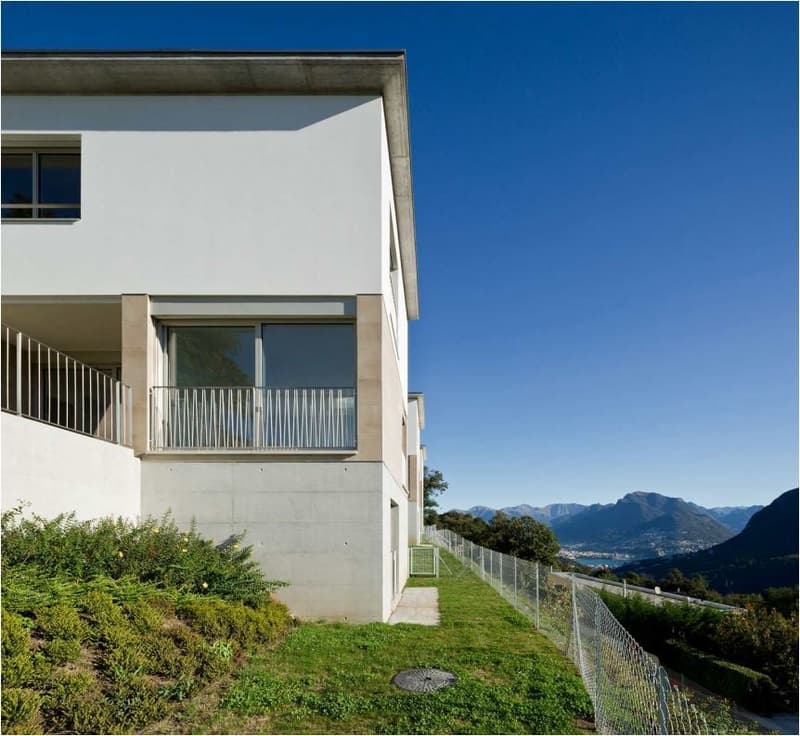 Multi-story apartment building with balconies, surrounded by greenery and with a scenic view of mountains in the background