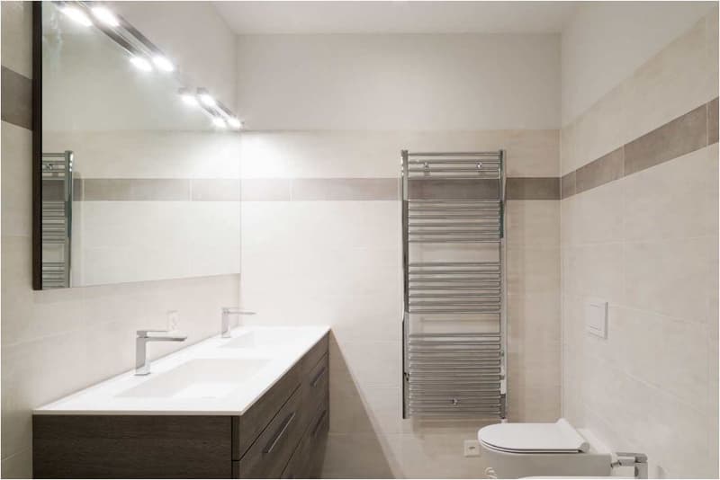 Spacious bathroom with white walls, large vanity with double sinks, and a chrome towel warmer on the wall.