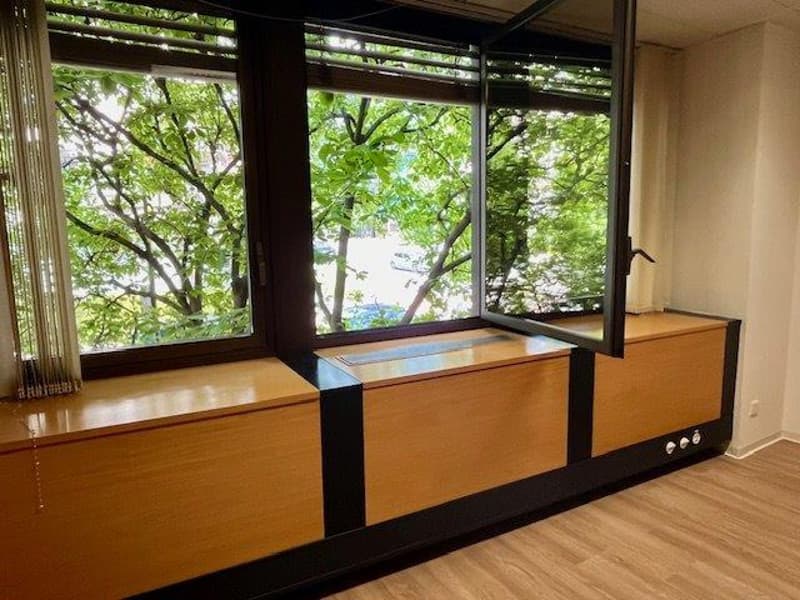 Large windows overlooking a lush, green outdoor area, wooden floors, built-in storage units or cabinets with a wooden finish.