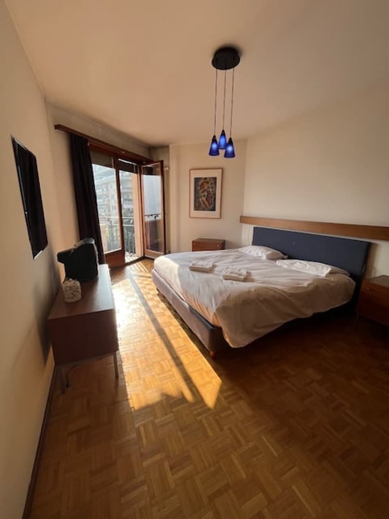 bed, wooden floor, blue bedding, wooden headboard, ceiling light, picture frame, table, television, sliding doors, balcony