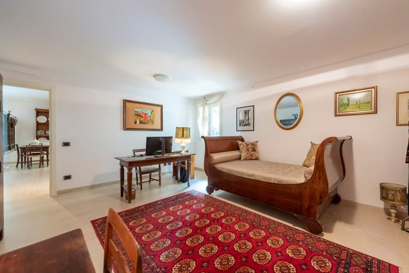 A room with a wooden bed, desk, chair, lamp, and rug. There are paintings on the wall, a mirror, and a cabinet in the corner.