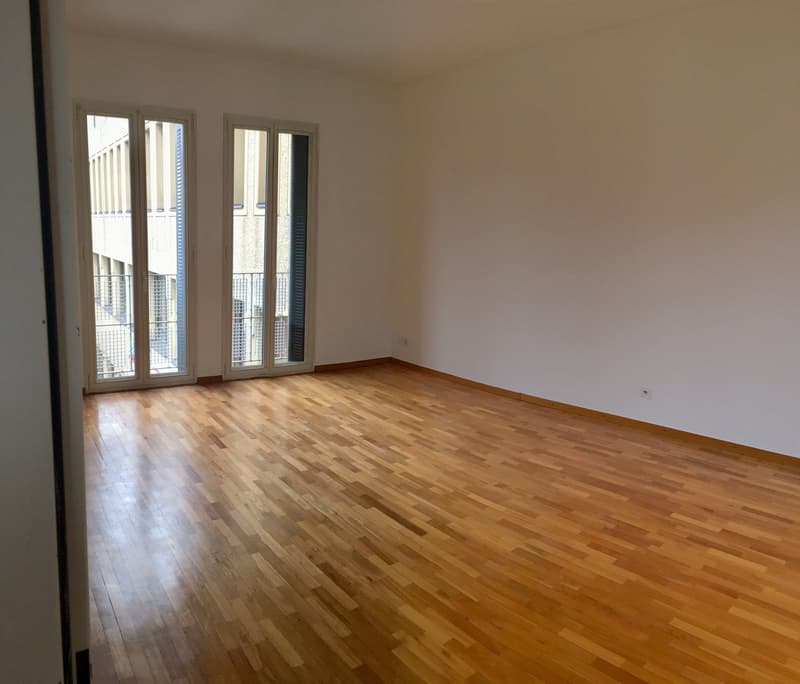 large open space, wooden floor, two double glass doors leading to balcony