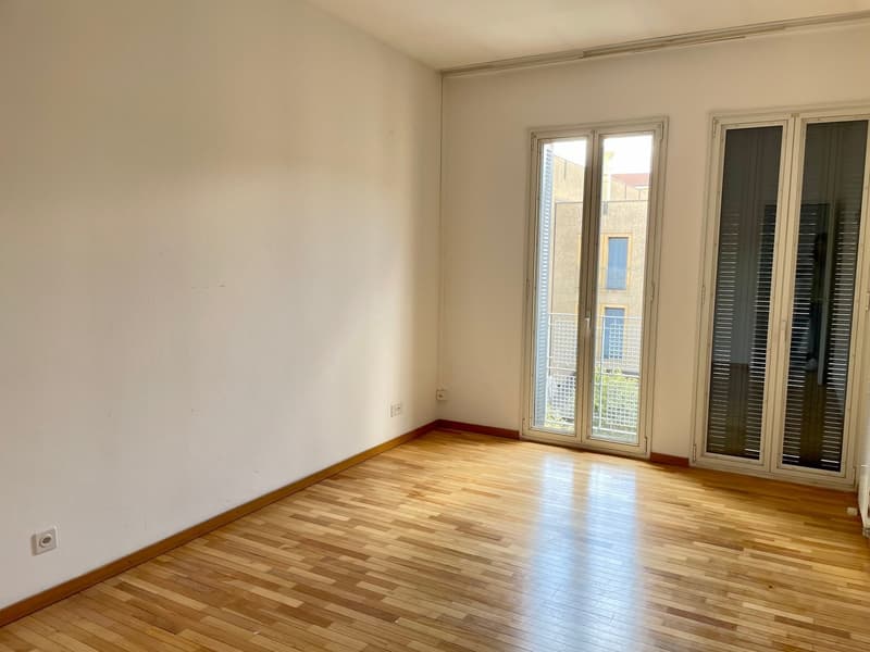 Empty room, white walls, wooden floor, glass doors leading to balcony