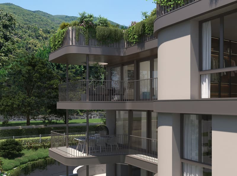 Modern multi-story apartment building with balconies overlooking a lush, green landscape. The building has a curved design with large windows and a terrace on the upper floors surrounded by plants and greenery.