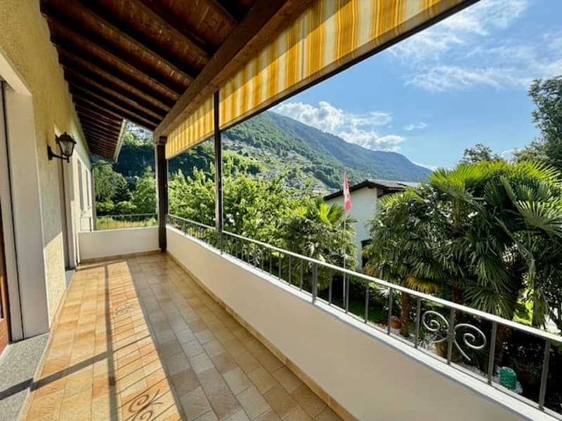 Terrace with awning, mountain view, railing, tiled floor, wall lamp, greenery