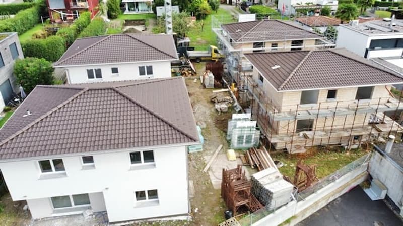 Multiple new build houses under construction, white exteriors, brown roofs, driveway, scaffolding around houses, construction materials scattered
