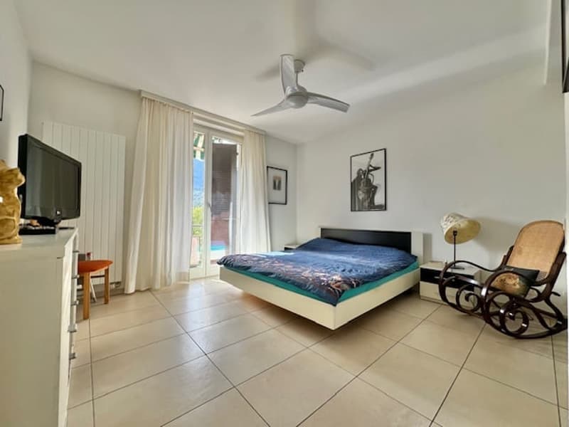 Spacious bedroom with white walls, tiled flooring, a large bed, a rocking chair, and a ceiling fan.