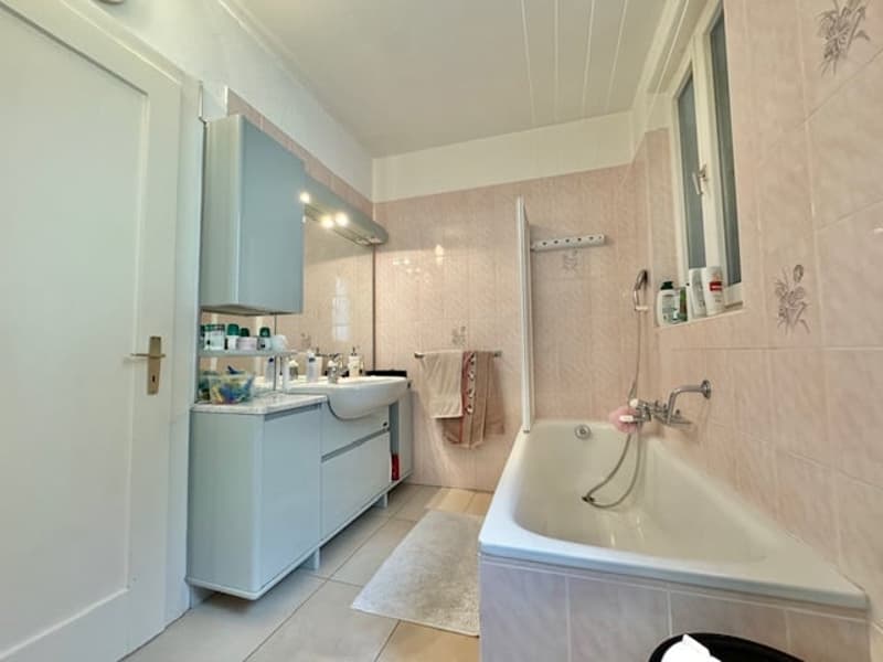The image shows a spacious bathroom with a bathtub, vanity with sink, and tiled walls. The room appears to be well-lit and has a clean, modern design.