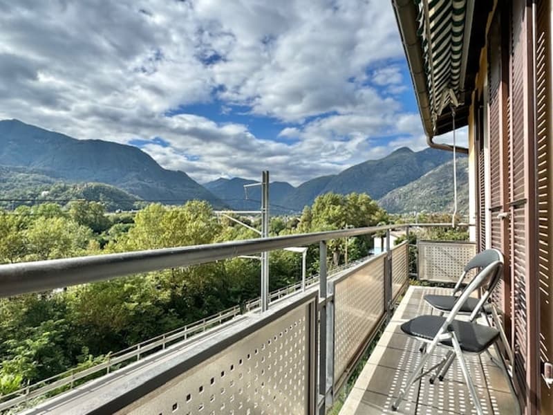 Spacious balcony with a panoramic view of the mountains and lush greenery. The balcony has a metal railing and chairs, providing a comfortable outdoor space to enjoy the scenic surroundings.