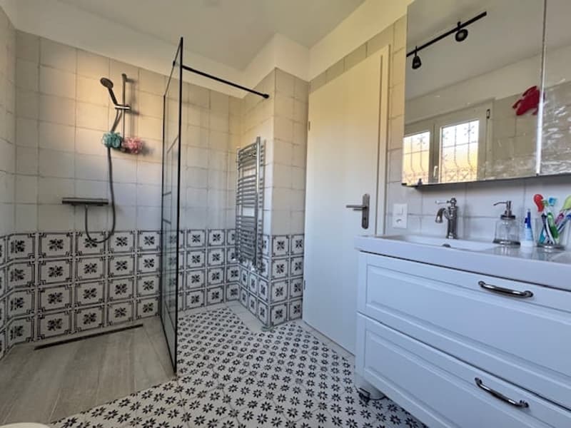 Spacious bathroom with tiled walls and floor, walk-in shower, vanity unit with drawers, and towel rack.