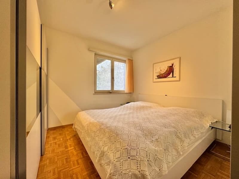 Bed with white bedding, a nightstand, a painting on the wall, a window with curtains, wooden floor