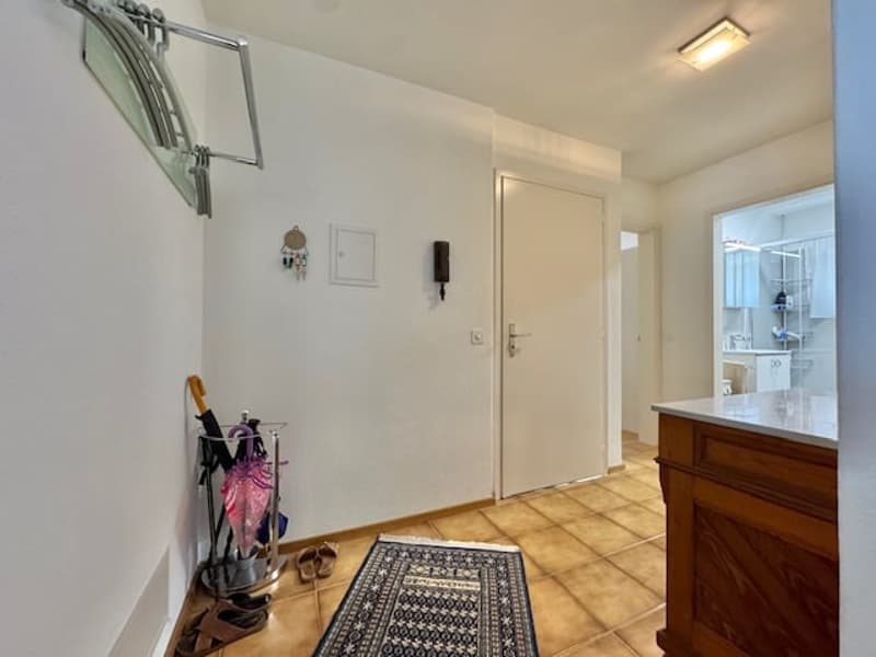 Entryway with tiled floor, white walls, an umbrella stand, a rug, and a white door leading to another room