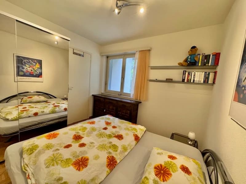 Bedroom with two single beds, bedside tables, mirrored wardrobe, nightstand, window, curtain, dresser, shelf with books, painting, ceiling lamp