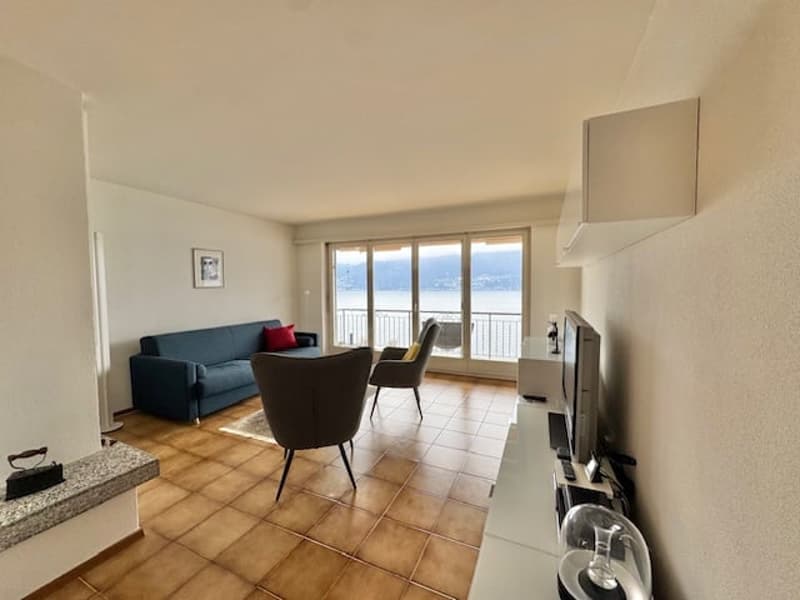 Spacious living room with large windows offering a view, hardwood floors, sofa, armchair, and TV stand.