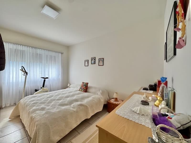 Spacious bedroom with a large bed, wooden furniture, and decorative items. The room has large windows that provide natural light and access to a balcony or terrace.