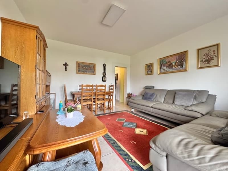 Spacious living room with hardwood furniture, including a large wooden dining table and chairs, as well as a gray sectional sofa. The room features a fireplace, religious artwork on the walls, and a patterned area rug.